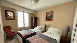 Una habitación de hotel con dos camas, una silla roja, un armario de madera y un cuadro en la pared.