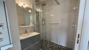 Un baño moderno con ducha de vidrio, tocador con espejo y suelo de baldosas.