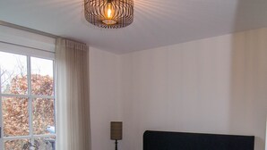 A bedroom with a bed, a nightstand, a lamp, and a window with curtains. - Rural B&B with a beautiful outdoor view and a village atmosphere! (Rhenen)