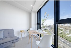 A modern room with a sofa, dining table, chairs, and a large window with a city view.