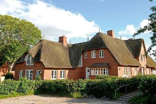Une maison traditionnelle en briques rouges, avec un toit de chaume et des fenêtres à cadre blanc.