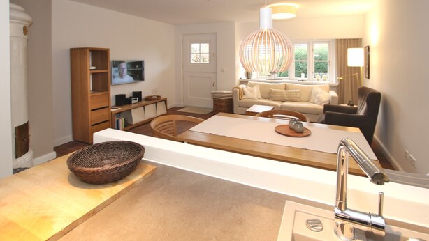 A modern living room with a kitchen area, a dining table, and a large window providing natural light. - Ferienwohnung in Wrixum, mit 3- Zimmern auf 60m² im Reetdachhaus (Wrixum)