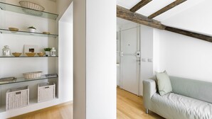 Ein modernes Interieur mit einer Glaseinheit zur Aufbewahrung, die Körbe und Dekoartikel zeigt, einem hellen Sofa und freiliegenden Holzbalken.