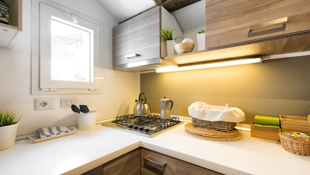 Eine moderne Küche mit Gasherd, Holzschränken, einem Fenster und einer Arbeitsplatte mit verschiedenen Küchenutensilien.