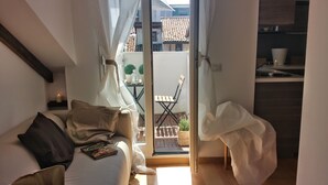 Ein gemütliches Zimmer mit einem Bett, einem kleinen Tisch mit Kerze und Blick auf einen Balkon mit Stuhl und Pflanzen.