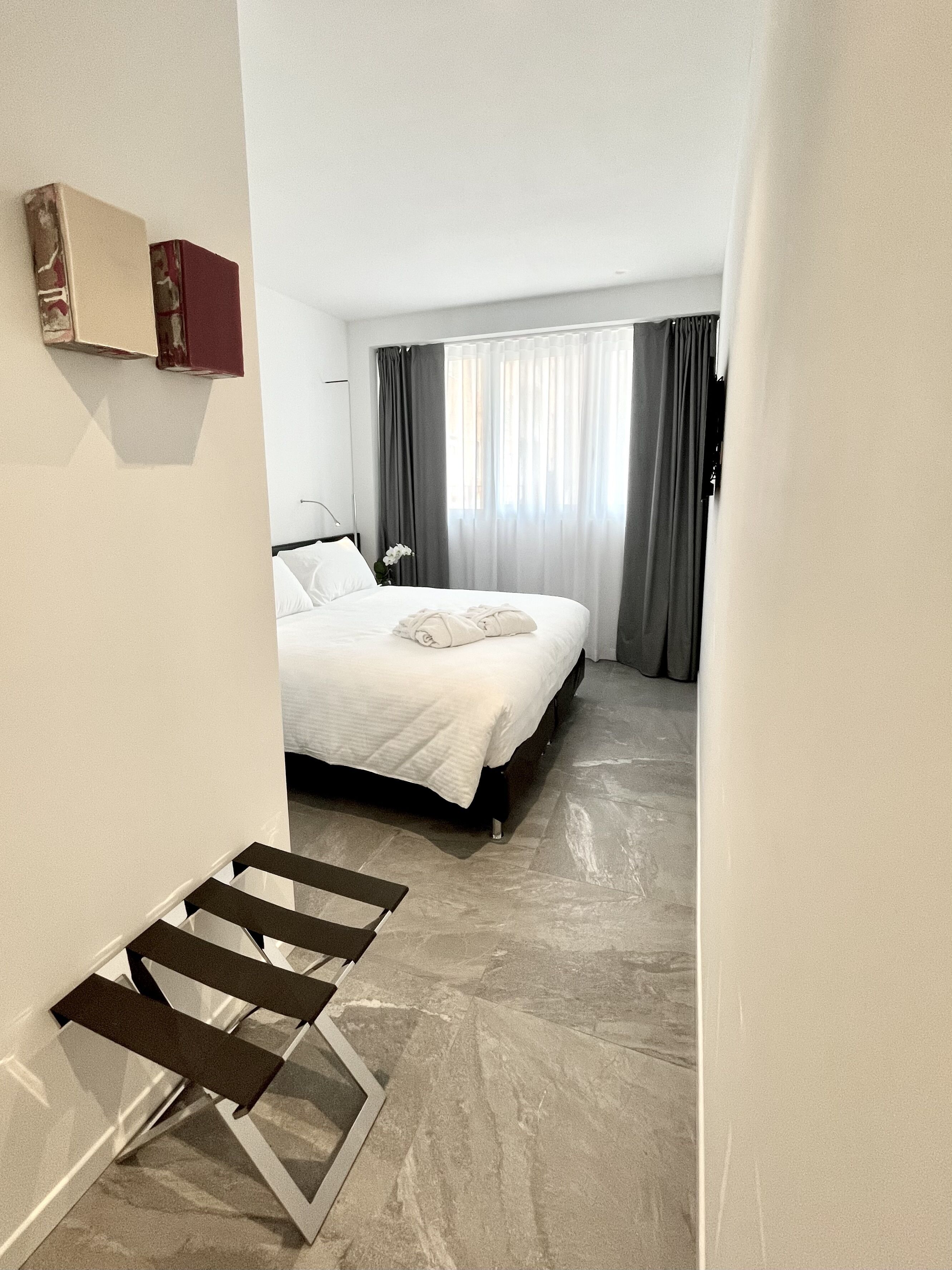 Une chambre d’hôtel moderne, équipée d’un lit, d’une petite table et offrant une vue sur l’extérieur à travers des rideaux transparents.