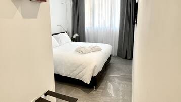 Une chambre d’hôtel moderne, équipée d’un lit, d’une petite table et offrant une vue sur l’extérieur à travers des rideaux transparents.
