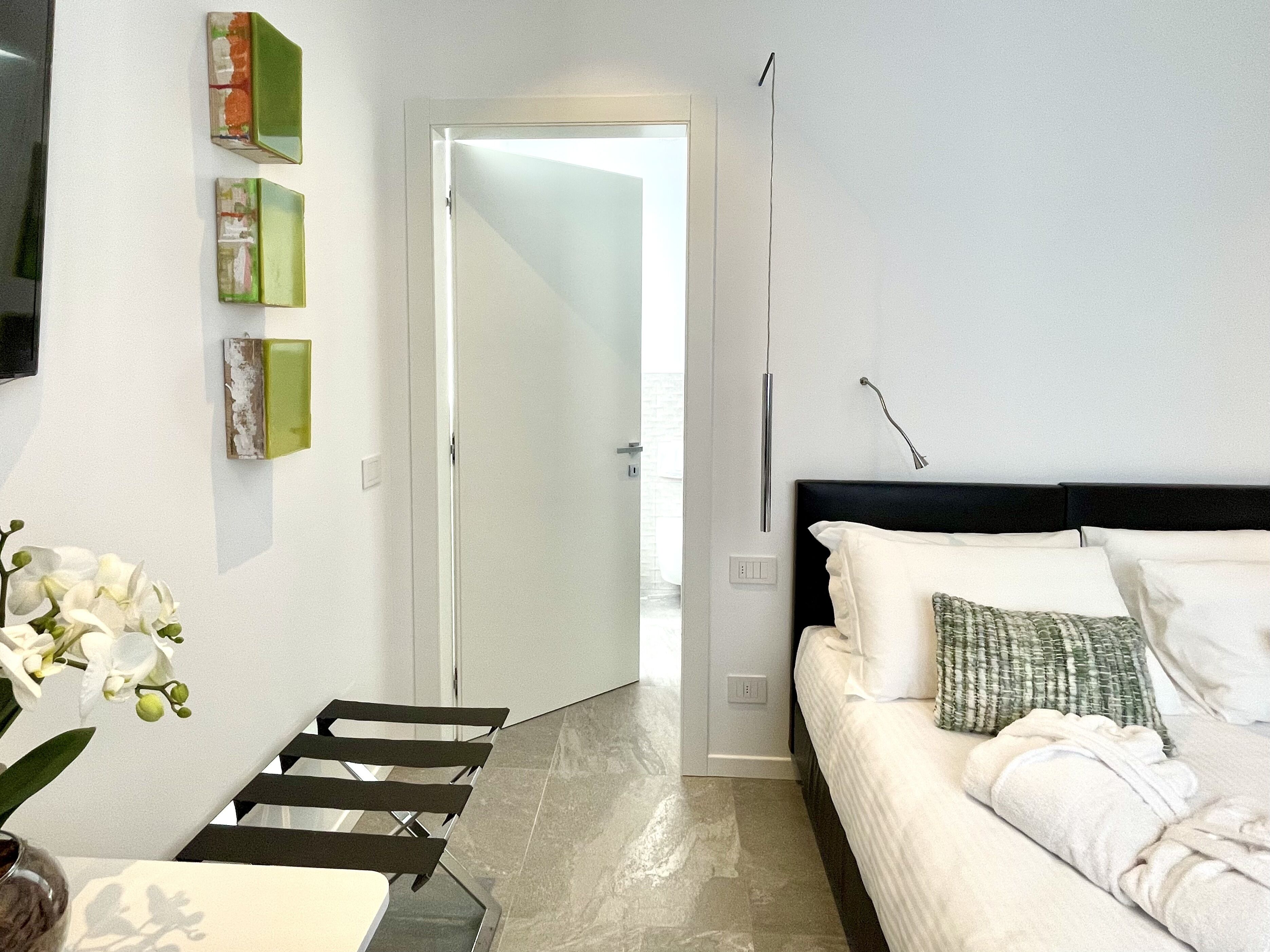 A modern bedroom with a bed, a chair, a small table, and a door leading to another room.