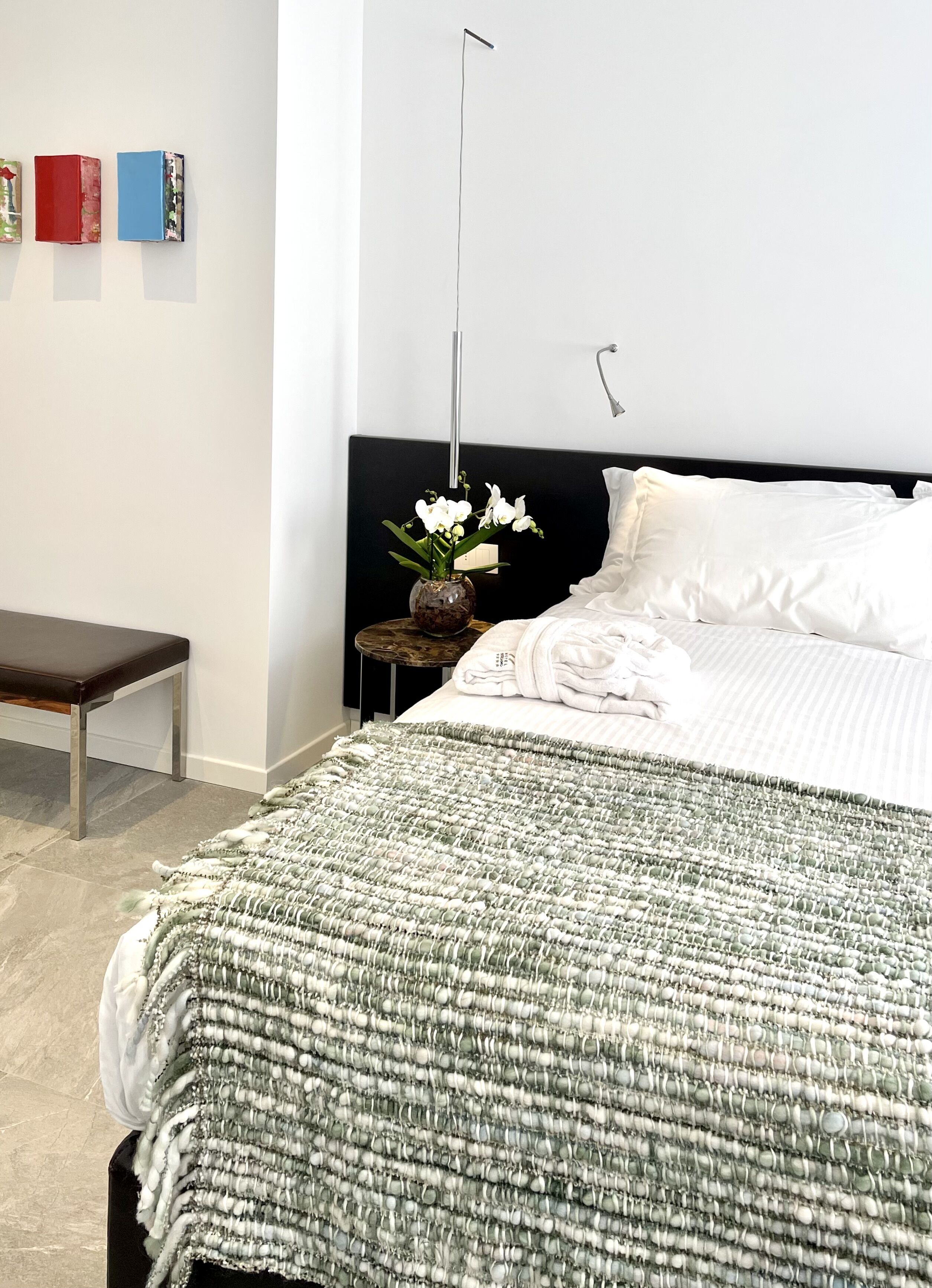 A bedroom with a bed, bedside table, bench, and a wall with three books.