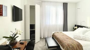 A modern hotel room with a bed, a desk, a chair, a TV, and a bathroom.