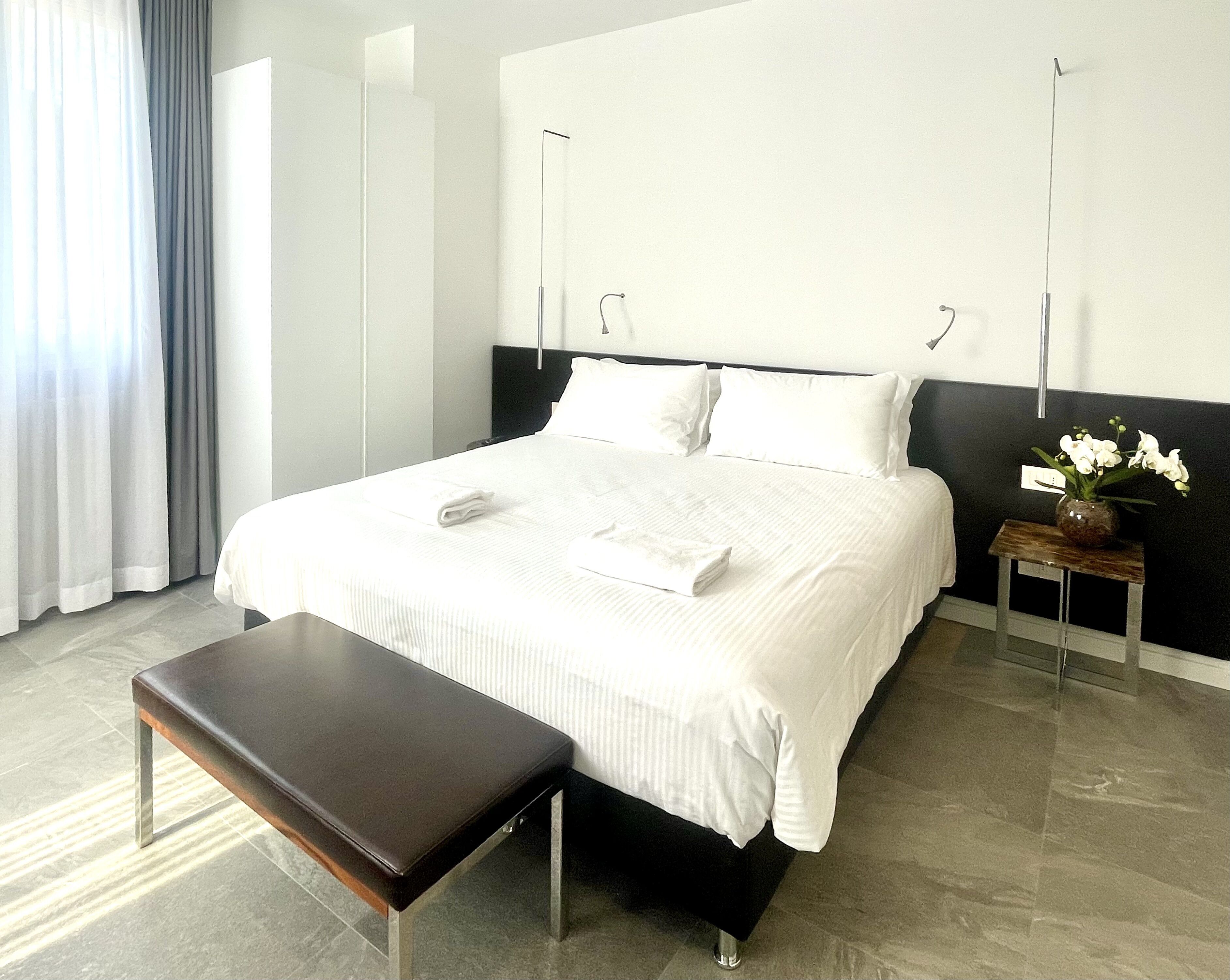 Una habitación de hotel moderna con una cama grande, una mesita de noche, un banco y un jarrón con flores.