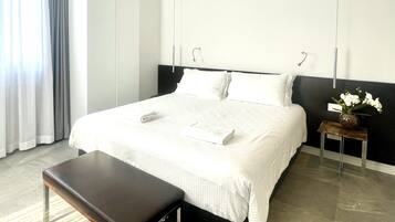 Una habitación de hotel moderna con una cama grande, una mesita de noche, un banco y un jarrón con flores.