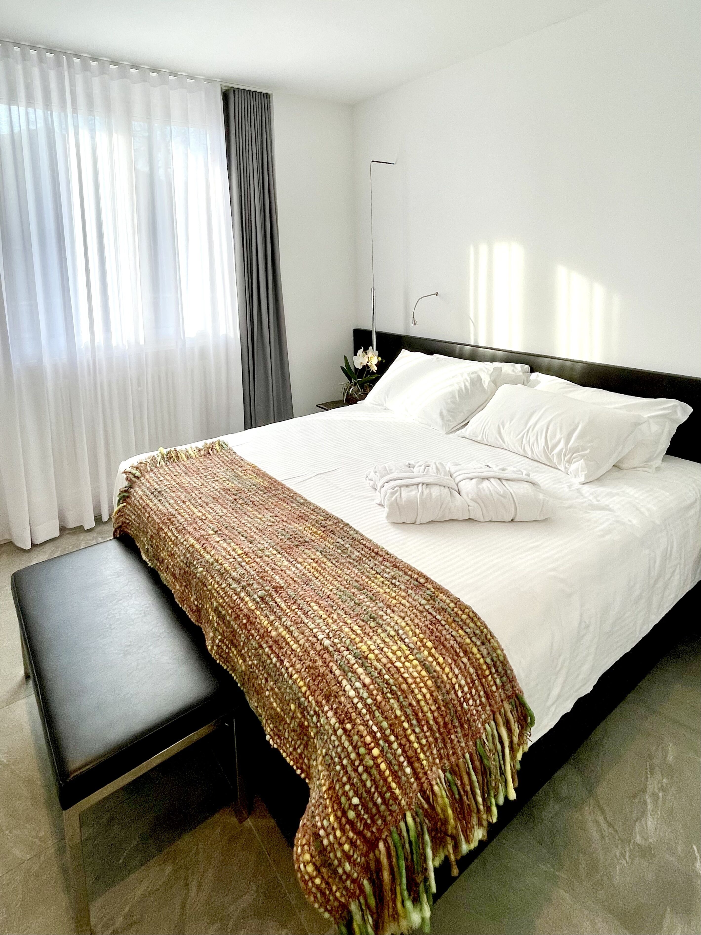 A neatly made bed with white linens and a brown woven throw blanket.