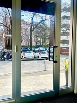 Vista attraverso un vetro su un'area di parcheggio con diverse auto e una strada sullo sfondo.