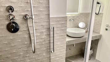 Et moderne badeværelse med et glasafskærmet brusebad, et rundt spejl og en hvid vask.