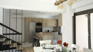 Une cuisine moderne avec des meubles en bois, un îlot central et un coin repas comprenant des chaises blanches et une table dressée pour quatre personnes.