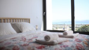 Une chambre avec une grande fenêtre, un lit recouvert d’une couette à motifs floraux et deux serviettes enroulées posées sur le lit.