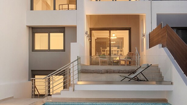 Une maison moderne à deux étages, dotée d’une piscine, d’un escalier et d’un coin repas visible à travers les fenêtres.