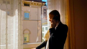 A person leaning on a window with a view of a building with arched windows and a bell tower. - Klemi (Trento)