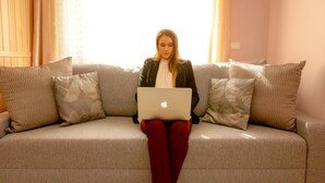 A person sitting on a grey sofa with a laptop, surrounded by patterned pillows. - Klemi (Trento)