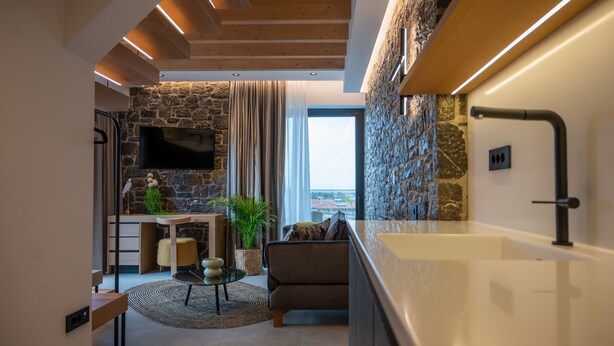 A modern living room with a stone wall, a flat-screen TV, a sofa, a coffee table, and a large bathtub. - Opal Executive Suites (Nafplio)