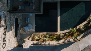 An aerial view of a modern outdoor living area with a pool, stone walls, and outdoor furniture. - Opal Executive Suites (Nafplio)