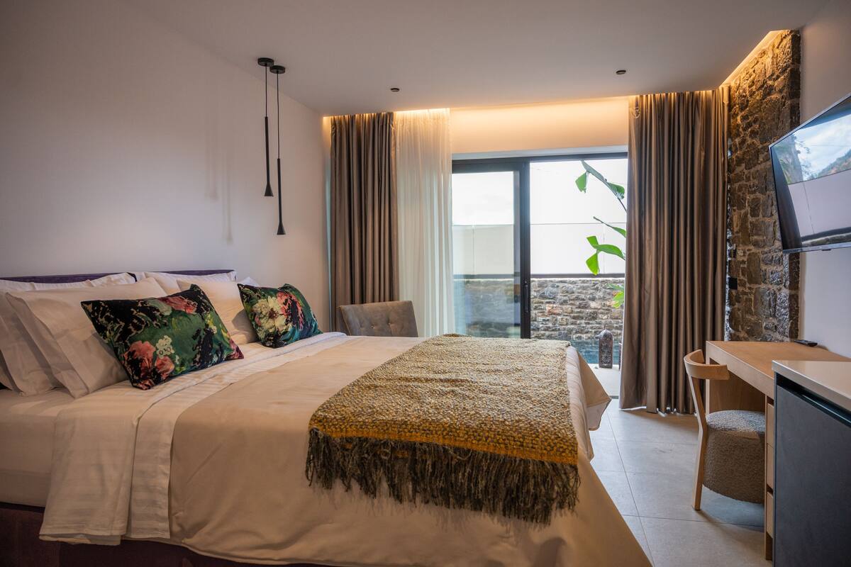 A bedroom with a bed, a desk, a TV, and a view of the outdoors.
