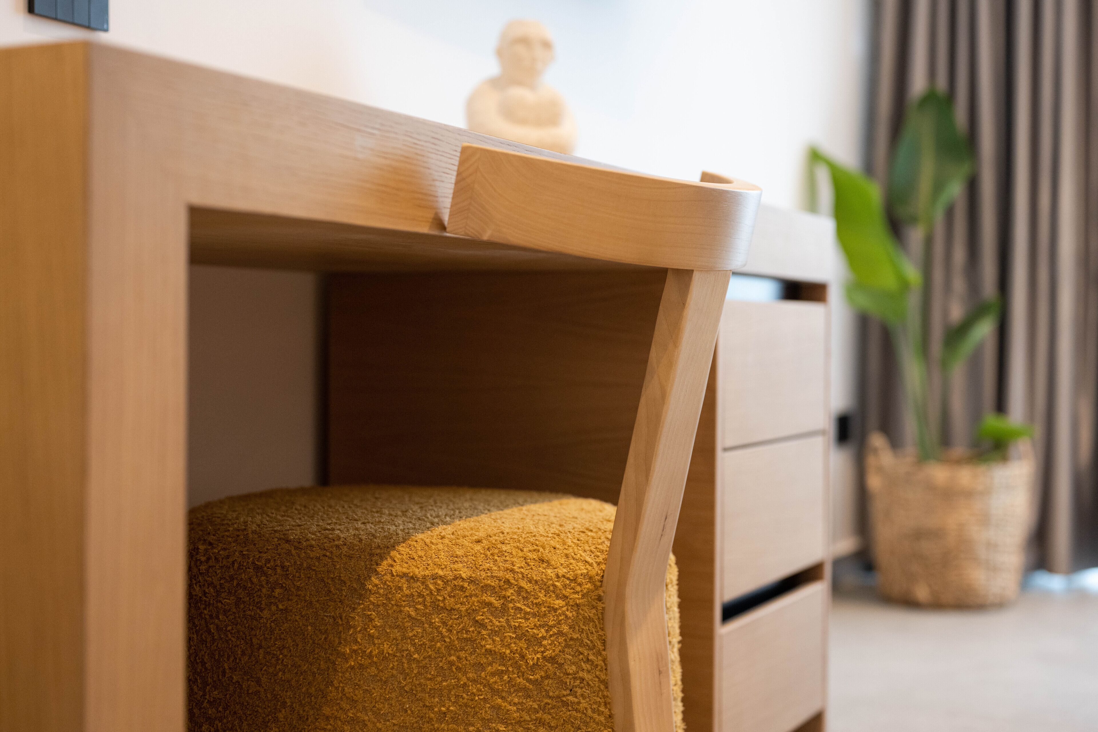 A wooden desk with a drawer, a small statue on top, and a plant in the background.