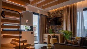 A modern living room with a staircase, a stone fireplace, and a flat-screen TV mounted on the wall. - Opal Executive Suites (Nafplio)