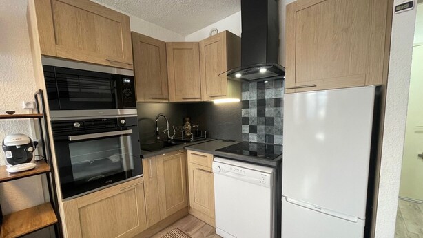 A compact kitchen with wooden cabinets, a black range hood, a white dishwasher, and a stainless steel refrigerator.