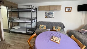 A bunk bed, a sofa, a table with a placemat, and a television on the wall.