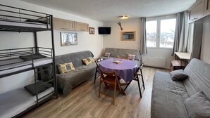A compact living space with bunk beds, a sofa, a dining table, and a TV.