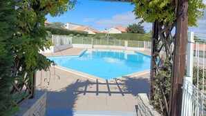 Uma piscina com pergolado, rodeada por vegetação e uma vedação.