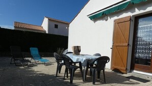 Um pátio com uma mesa, cadeiras, uma porta de madeira e uma parede branca.