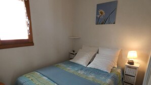 Quarto com cama, mesa de cabeceira, abajur e janela.