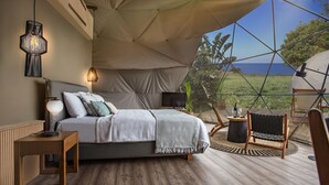 A tented accommodation room with a bed, bedside lamp, and a view of the outdoors. - Eco Dome Crete (Agios Nikolaos)