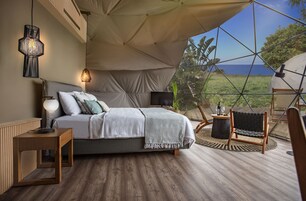 Habitación tipo alojamiento en tienda de campaña con cama, lámpara de noche y vistas al exterior.