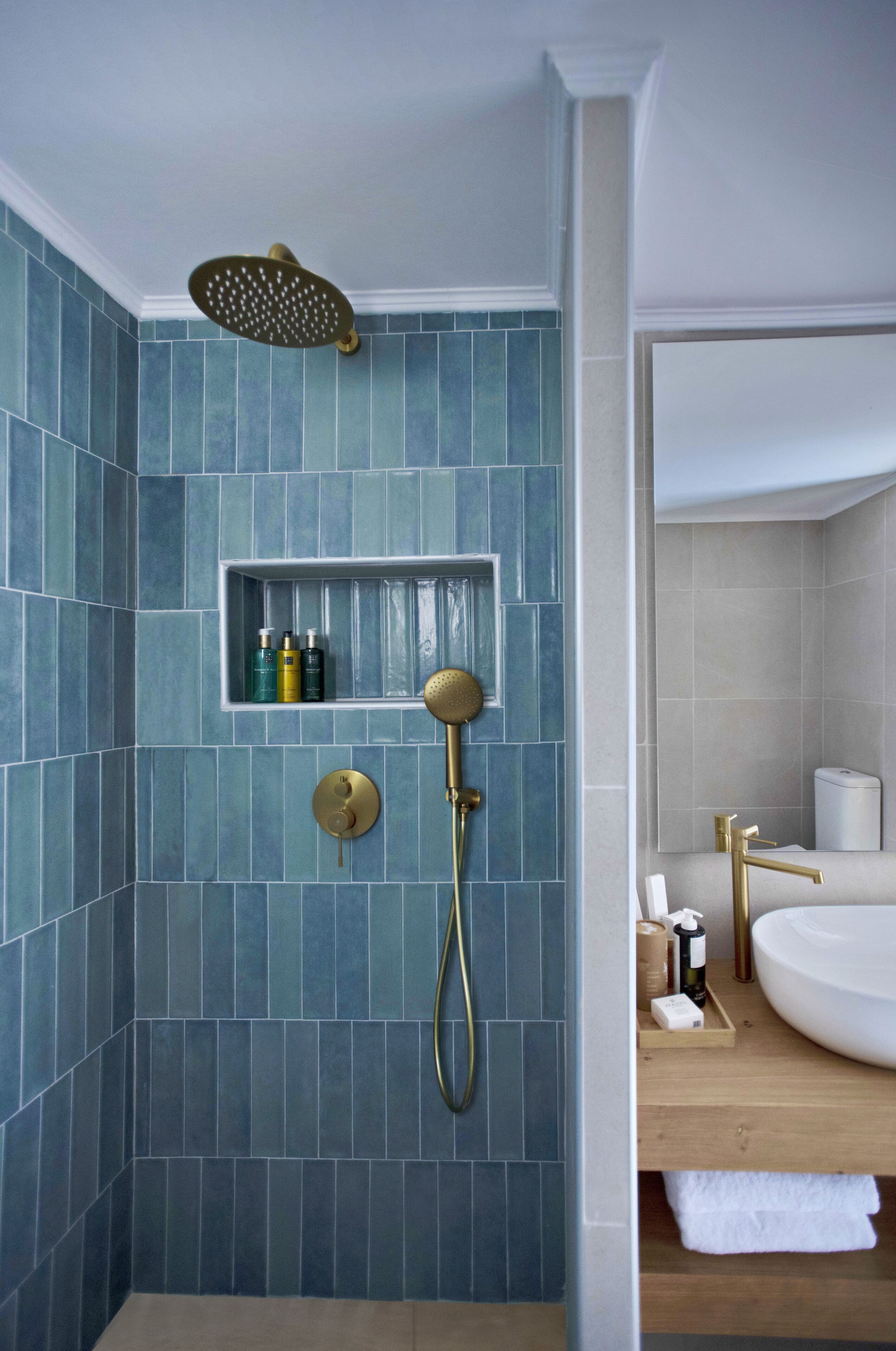 Un baño moderno con azulejos azules, un cabezal de ducha dorado y un lavabo blanco.