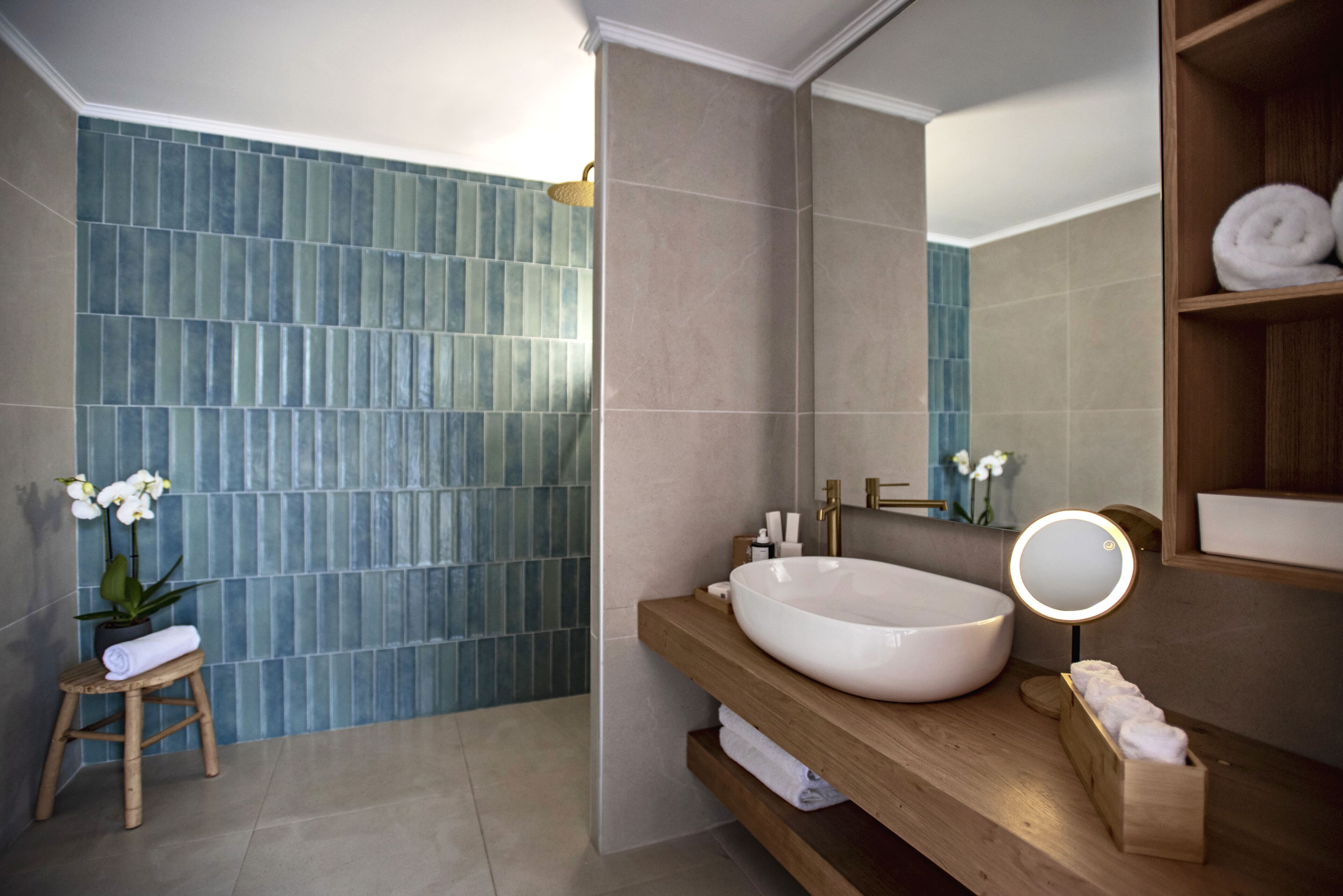 A modern bathroom with a large white sink, wooden vanity, and a blue-tiled shower area.