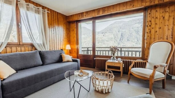 Ein gemütliches Zimmer mit einer Couch, einem Sessel, einem kleinen Tisch und einem Korbwäschesessel.