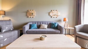 A modern living room with a grey sofa, a coffee table, and two wall-mounted wooden art pieces. - Charming historical house, pets allowed, private parking (Vicq-sur-Mer)
