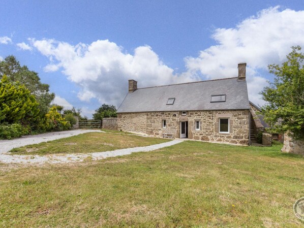 A stone farmhouse with a gravel driveway, a small front porch, and a clear sky.