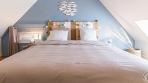 A bedroom with a sloped ceiling, a bed with white bedding, a wooden headboard, and a wall-mounted light fixture. - Charming historical house, pets allowed, private parking (Vicq-sur-Mer)