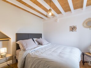 A bedroom with a bed, bedside table, lamp, and a hanging light fixture.