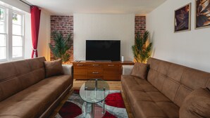 A living room with two brown sofas, a glass coffee table, a flat-screen TV on a wooden cabinet, and a red and gray patterned rug.