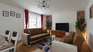 A living room with a brown sofa, a glass coffee table, a TV, and a brick wall.