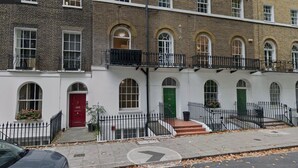 A row of townhouses with white facades, arched windows, and a black metal fence.