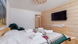 Ein Schlafzimmer mit Holz-Kopfteil, einem an der Wand montierten Flachbildfernseher, einem Bett mit weißen Leinen und einer dekorativen Decke sowie einem Bild an der Wand.