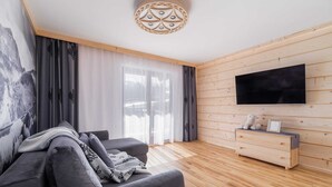 Ein modernes Wohnzimmer mit einer Couch, einem an einer Holzwand montierten Fernseher und Holzboden.