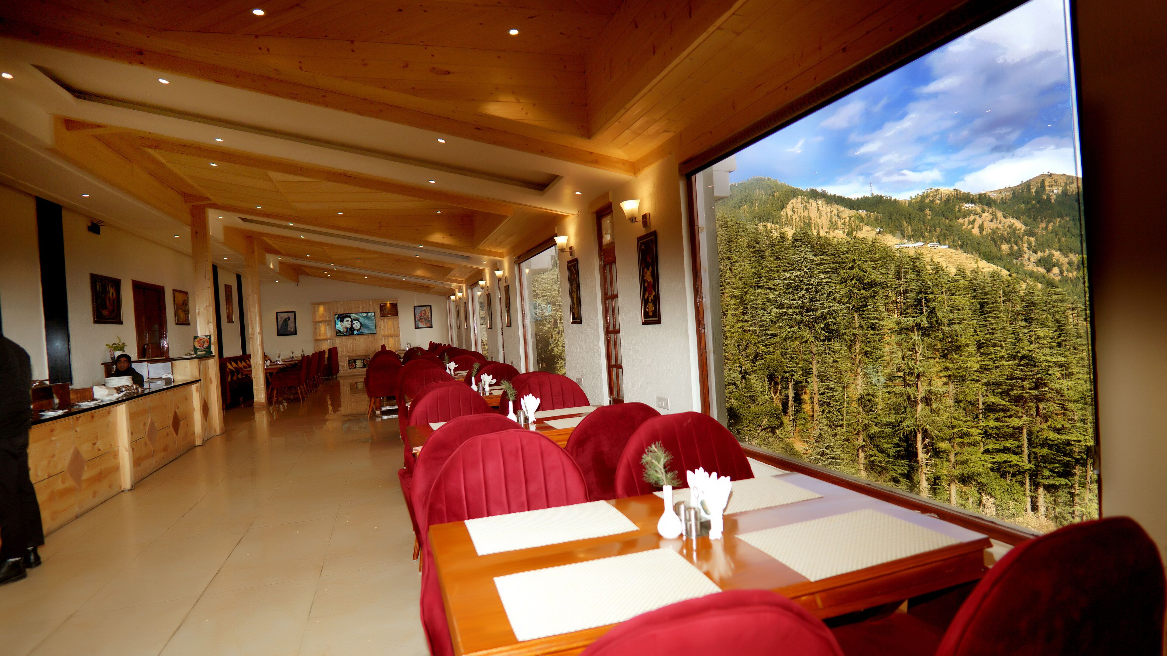 Un ristorante con interni in legno, sedie imbottite rosse e vista su una montagna boscosa.